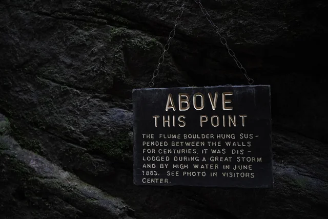 A sign reading "Above This Point" attached to a dark rock wall.