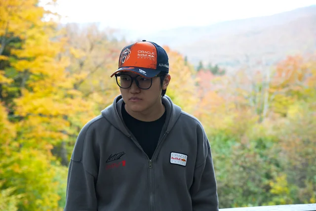 A person in an orange cap with autumn hills in the background.